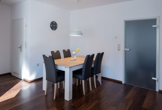 Esszimmer mit einem Holztisch und sechs schwarzen Stühlen, hell und modern eingerichtet.