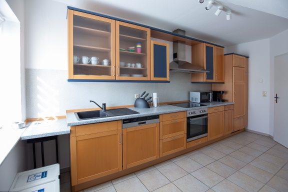 Moderne Küche mit Holzschränken, Edelstahlgeräten und Fliesenboden.