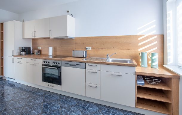Moderne Küche mit Holz- und weißen Elementen, ausgestattet mit Herd, Kühlschrank und Ablagen.