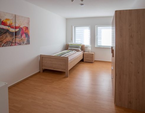 Helles, minimalistisches Schlafzimmer mit einem einzelnen Bett und einem Schrank.