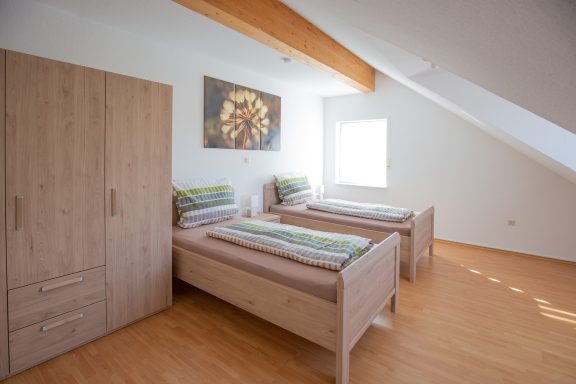 Helles Schlafzimmer mit zwei Betten, Holzschrank und modernem Wandbild.